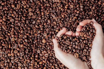 Coffee beans in man palms in form of a heart on coffee background