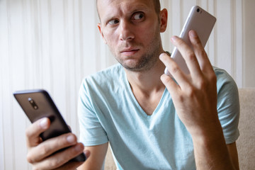 the guy with two smartphones in his hands with amazement looks at the screen