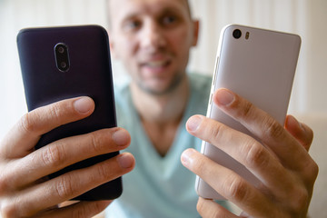 guy with two smartphones in his hands with a smile looks at the screen
