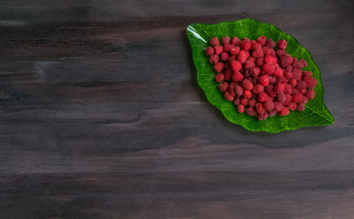 Ripe raspberry in a plate in the form of a green leaf on a black wooden background.