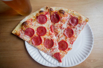 two slices of pepperoni pizza on a plate with a beer