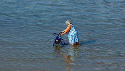 Elderly lady walks with walker in the sea.