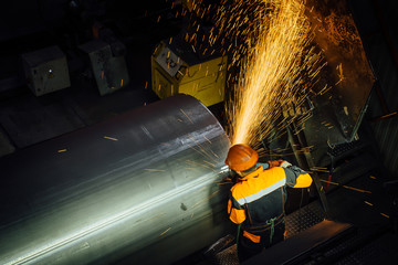 Worker cleans welded seam on steel pipe using grinding machine in metalwork workshop