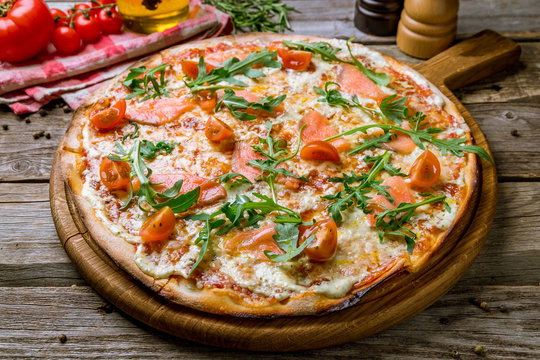 Pizza with salmon, tomatoes and aragula on wooden background