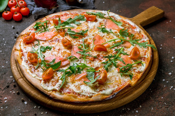 Pizza with salmon, tomatoes and aragula on dark concrete rustic background