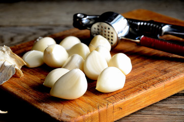 Fototapeta na wymiar Peeled garlic cloves and garlic masher on a wooden kitchen cutting board.