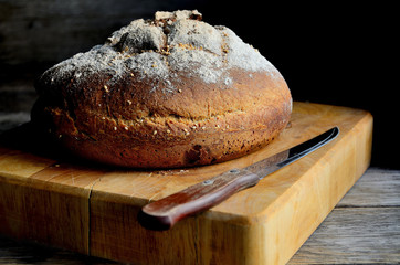 Round loaf of homemade bread with sesame on a wooden old table.