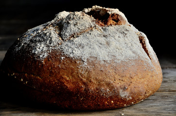 Round loaf of homemade bread with sesame on a wooden old table.