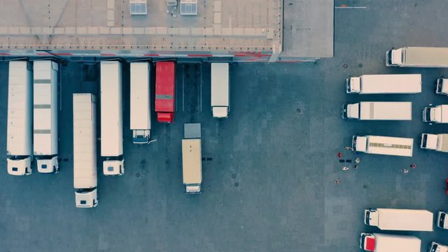 Aerial top view of many semi-trailers trucks standing for load/unload goods  at the ramps of warehouse on logistics park with loading hub