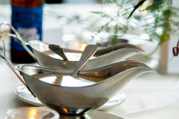 detailed shot of luxury silver gravy bowls containing salad dressing at a banquet for a wedding party.  the romantic dinner is elegant with white table cloth and decorative plate wear