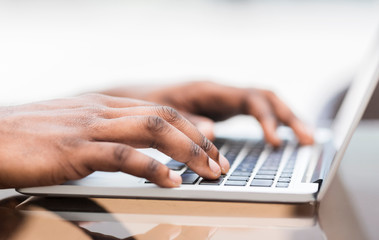 Close up of young african american guy typing on laptop