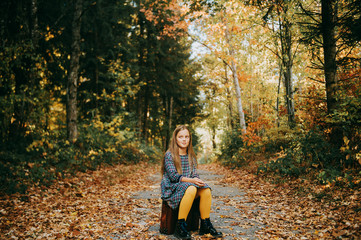 Autumn portrait of pretty young girl with old vintage suitcase, kid model posing outdoor in the forest, wearing plaid dress and yellow tights