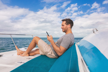 Boat man using mobile phone texting on satellite internet while relaxing on deck of yacht luxury lifestyle.