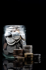 stack of coin and clear jar with thai baht coin on black background. concept for financial and saving money
