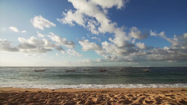 Picturesque voew of a few jukungs, small wooden Indonesian outriggers canoes, waving on ocean surface. Sandy beach, amazing cloudscape. Morning. Bali, Indonesia. 