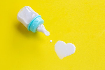 Bottle of milk for baby on yellow background. Milk heart shape