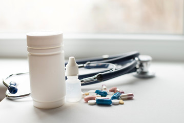 Stethoscope with medical equipment and pills on white background, close up