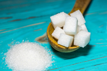 Refined sugar in a wooden spoon with loose sugar on a blue wooden background.