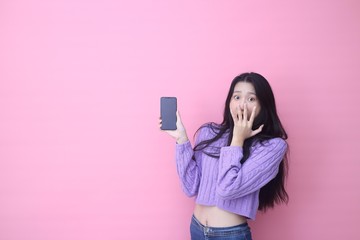 Naklejka premium happy excited glad to receive text message informing about salary, rejoices good news, stares at mobile phone, actively from happiness, Beautiful Asian models over pink background for advertising c