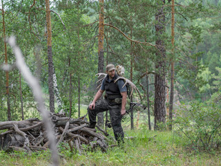 A hunter with a bow walks through the woods and carries elk or deer antlers on his back....
