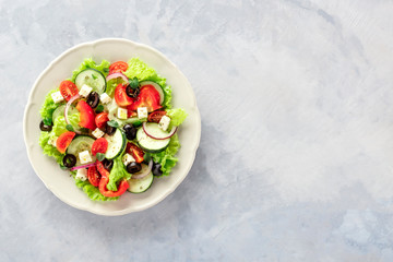 Greek salad. An overhead photo of a plate of fresh salad with lettuce, feta cheese, tomatoes, cucumbers, onions and olives, with copyspace