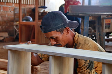 Carpenters work on woodworking machinery at carpentry shops making bookshelves. Photographed in part focus, blurry background, in a room with minimal light, Malang Indonesia, June 26, 2019