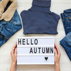 Set of female autumn clothes, female hands holding lightbox with 'Hello autumn' words. Overhead view, from above, flat lay.