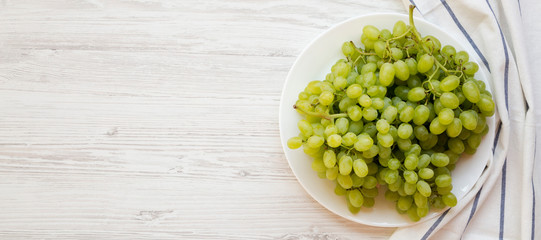 Green grape on a white plate over white wooden surface, top view. Space for text.