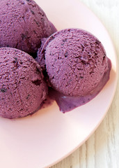 Blueberry ice cream balls on a pink plate on a white wooden background, side view. Close-up.