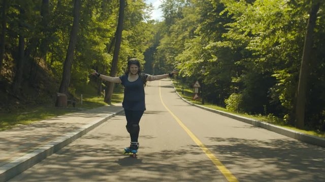 Excited woman rollerblading down road holding hands like wings enjoying extreme, freedom, speed on sunny summer day. Happy female in protective outfit riding downhill while headwind blowing in face.