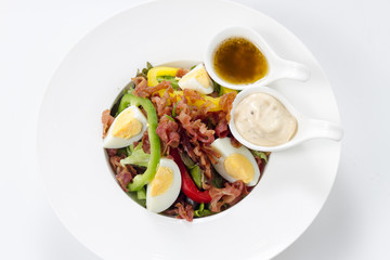 Fresh Caesar Salad with Deep-fried Bacon and Boiled Eggs & Mayonnaise on White Porcelain Circle Dish, Isolated on White Background with Shadow. Close-up Top View, Selective Focus at Food.