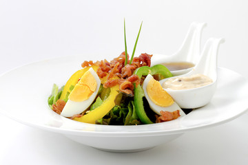 Fresh Caesar Salad with Deep-fried Bacon, Boiled Eggs & Mayonnaise, Italian dressing on White Porcelain Circle Plate, on White Background with Shadow. Close-Up Low Angle Side View, Focus at Food.