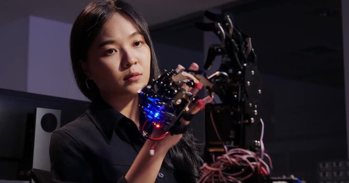 Asian testing cyborg hand at control room. Female doing her robot project she testing sensor signal. Technology and innovation concept.