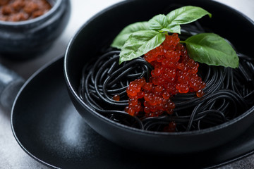 Close-up of a black bowl with squid-ink spaghetti, red caviar and fresh green basil, selective focus