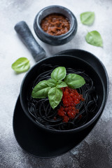 Spaghetti with squid-ink, red caviar, sun dried tomato pesto and green basil, elevated view over grey stone surface