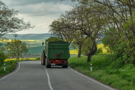 transport of fodder in a large trailer, tractor transports freshly cut grass to a farm, winding road on the hills in Moravia