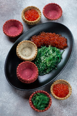 Vegetable tartlets with red caviar and seaweed salad, studio shot on a light grey stone surface