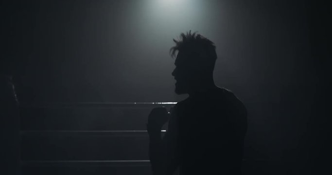 Male boxer training in the dark ring. Slow motion. Silhouette. Boxing concept.