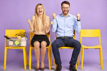 happy young blonde woman with closed eyes and man in round eyewear sitting extremely excited by great news and waiting for job interview