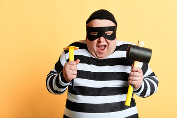 cheerful thief with wide open mouth using tools to break into the house, isolated yellow background. studio shot