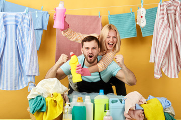 woman and man shouting with happiness, crazy and yelling with raised hands, crazy housekeepers celebrating success. couple found effective washing liquid, deterget. studio shot. yellow background