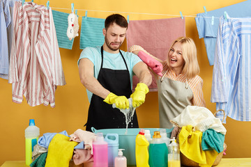 cheerful positive blonde woman leaning on man's shoulder and checking his work in the laundry room with yellow wall, close up portrait. lifestyle. free time, spare time, family doing household chores