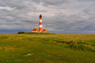 Fototapeta na wymiar Lighthouse Westerheversand on the peninsula Eiderstedt in the midst of salt grass in front of a dramatic cloudy sky