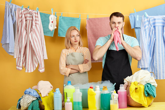 handsome bearded man in black apron and blue T-shirt inflating balloon while his girlfriend with crossed arms looking at him with unhappy expression. close up portrait - Powered by Adobe