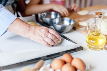 Fototapeta na wymiar Cooking process. Family is cooking in cozy home kitchen. Eggs, oil, baking paper and ingredients are on table. Graceful hands of senior woman and child prepare autumn pastries for dinner