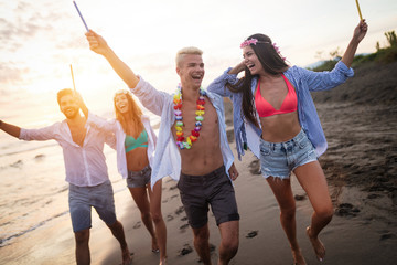 Obraz premium Happy group of friends lighting sparklers and enjoying freedom at beach during sunset