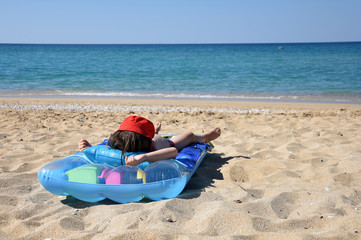 Fototapeta na wymiar Child relax on inflatable mattress at beach. Child with a red hat lies on beach