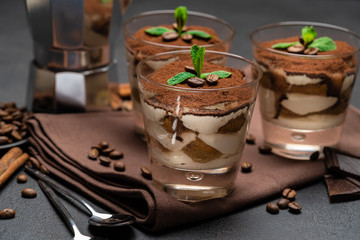 Classic tiramisu dessert in a glass and coffee maker on dark concrete background