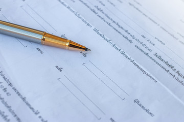Low angle view of golden pen lying on white sheet of paper in a folder with another set of paperwork