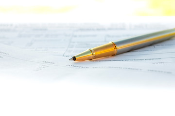 Low angle view of golden pen lying on white sheet of paper in a folder with another set of paperwork